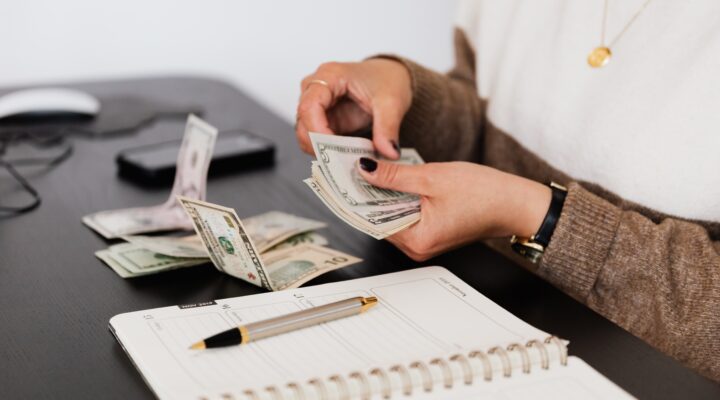 A person counting money with a book and pen on the table for budgeting