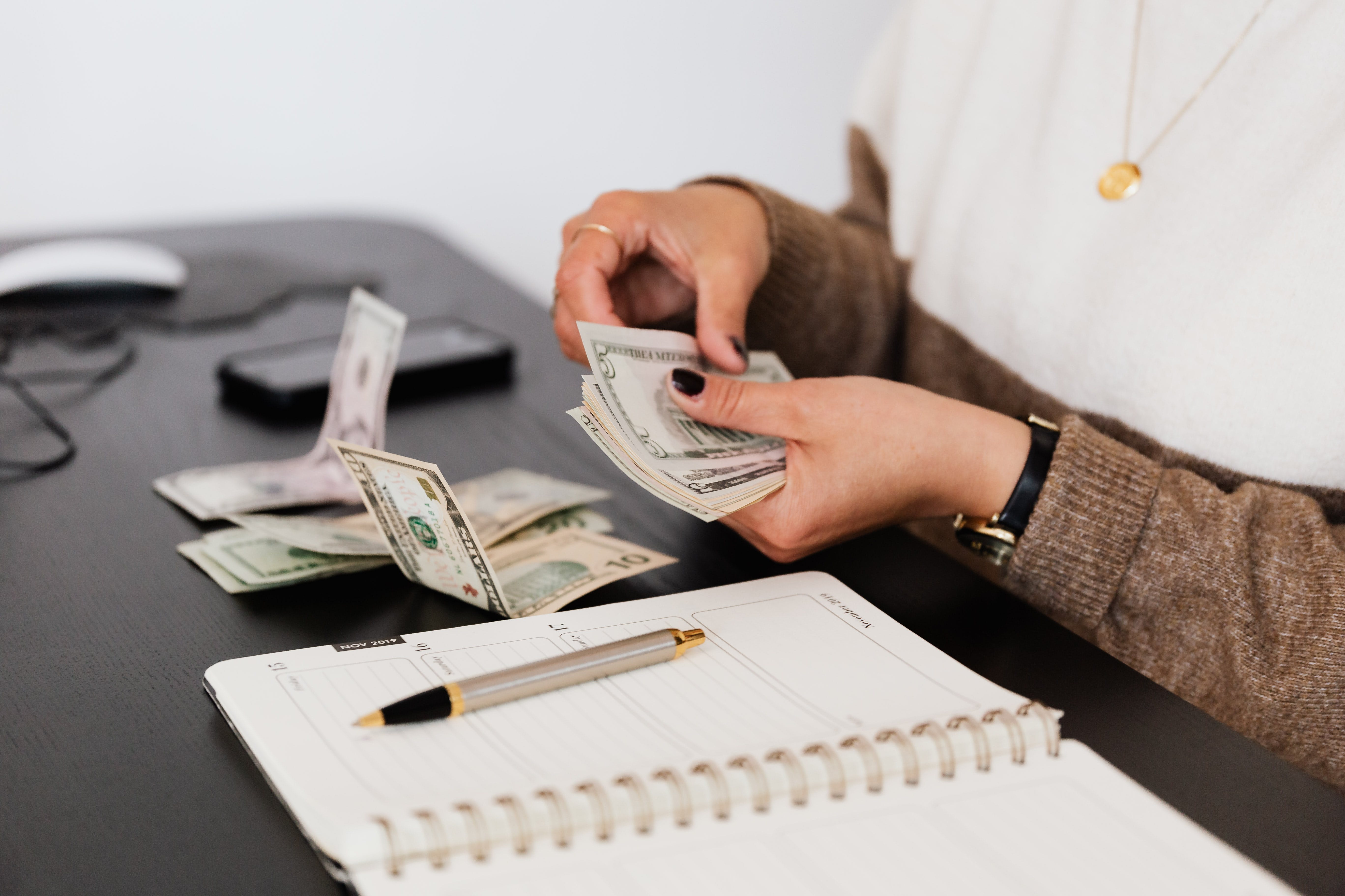 A person counting money with a book and pen on the table for budgeting