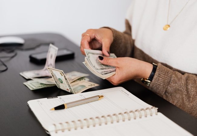 A person counting money with a book and pen on the table for budgeting